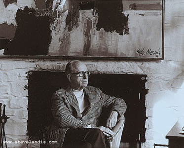 James Michener in front of fireplace seated, looking right