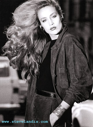 Jerry Hall, wind blowing her long hair, wearing an outfit by Donna Karan, in a black and white fashion photo shot outdoors on a Manhattan street