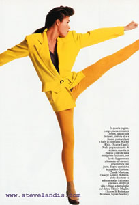 Karina Lombard kicking in the air, wearing a yellow jacket over mango stretch capris in a studio fashion photo by Steve Landis